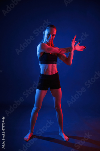 Preparing for sportive exercises. Warm up exercises. Beautiful muscular woman is indoors in the studio with neon lighting © standret