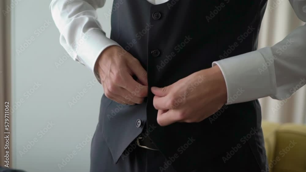 A man is fastening a button on a black jacket or vest. Male wears a classic suit. Businessman, office worker or groom. A man is fastening a button on a black jacket or vest. Male wears a classic suit. Businessman, office worker or groom.