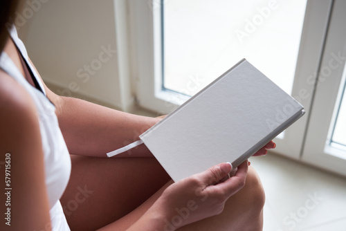 Wallpaper Mural Young woman holding blank notebook or book mockup with white cover while sitting on the bed. Torontodigital.ca