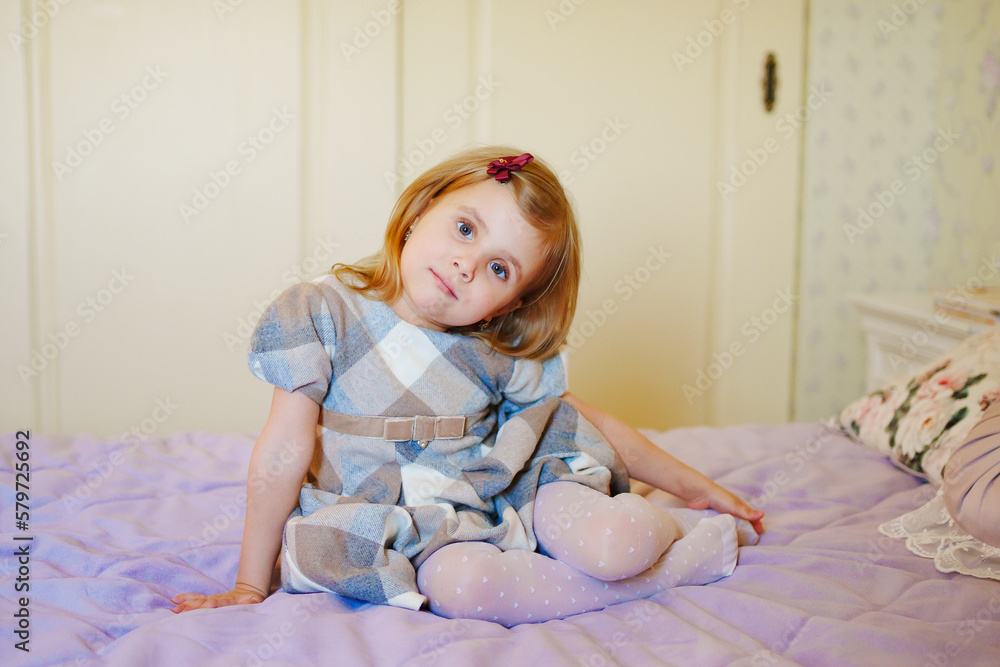 Fototapeta premium a portrait of a cute little girl in a plaid dress in the bed. 