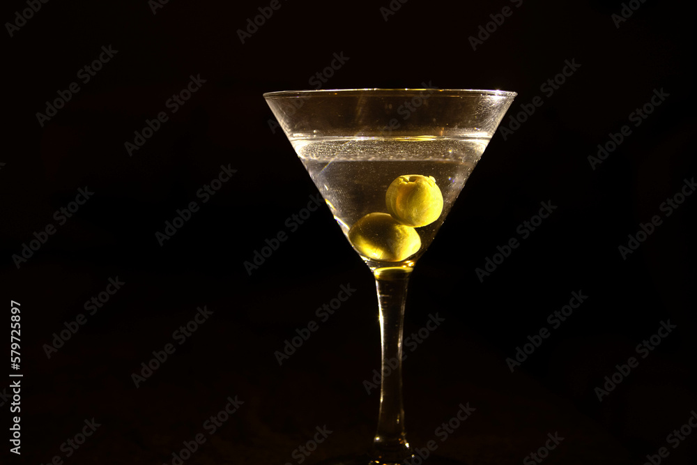 A clear glass of martini, focus on olives on a night club marble bar counter 