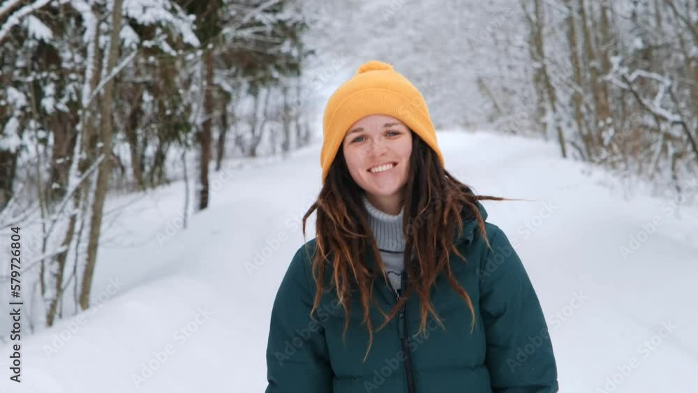 Portrait of happy girl in winter forest close up. Young blue-eyed Caucasian woman wears sweater and yellow hat, stands in snowy park and laughs with teeth smile. Front view. Female with dreadlocks. Portrait of happy girl in winter forest close up. Young blue-eyed Caucasian woman wears sweater and yellow hat, stands in snowy park and laughs with teeth smile. Front view. Female with dreadlocks.