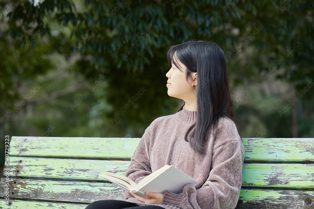 Obraz premium 春の公園で読書しながらコーヒーを飲む女子中学生の姿