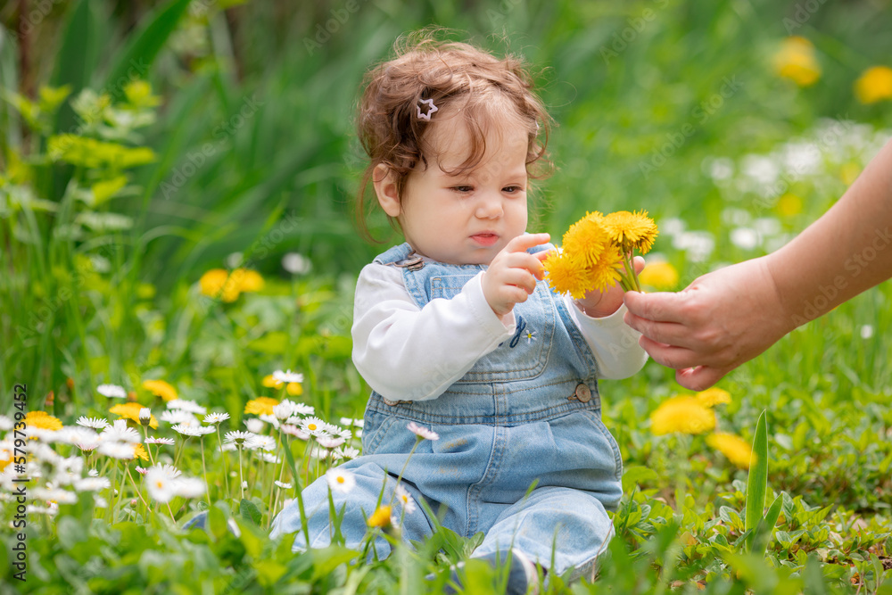 Happy little baby girl sitting on a green meadow with yellow flowers dandelions on the nature in the park Happy little baby girl sitting on a green meadow with yellow flowers dandelions on the nature in the park