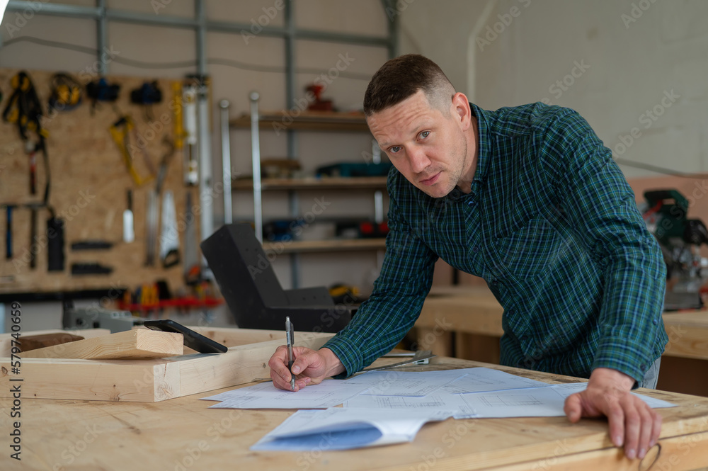 Portrait of a carpenter in a plaid shirt draws a workshop blueprint. Portrait of a carpenter in a plaid shirt draws a workshop blueprint.