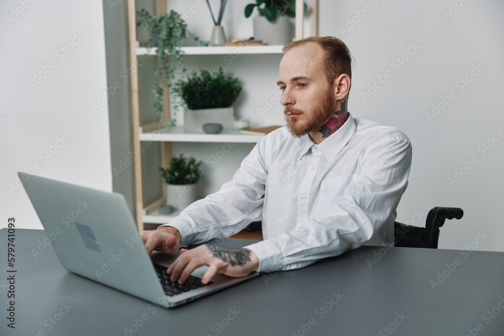 A man in a wheelchair a businessman with tattoos in the office works at a laptop, integration into society, the concept of working a person with disabilities, freedom from social frameworks A man in a wheelchair a businessman with tattoos in the office works at a laptop, integration into society, the concept of working a person with disabilities, freedom from social frameworks