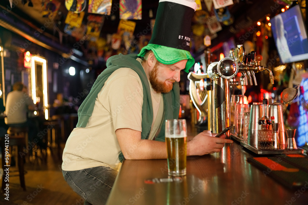 ginger man wearing leprechaun hat for st. patrick's day using smartphone