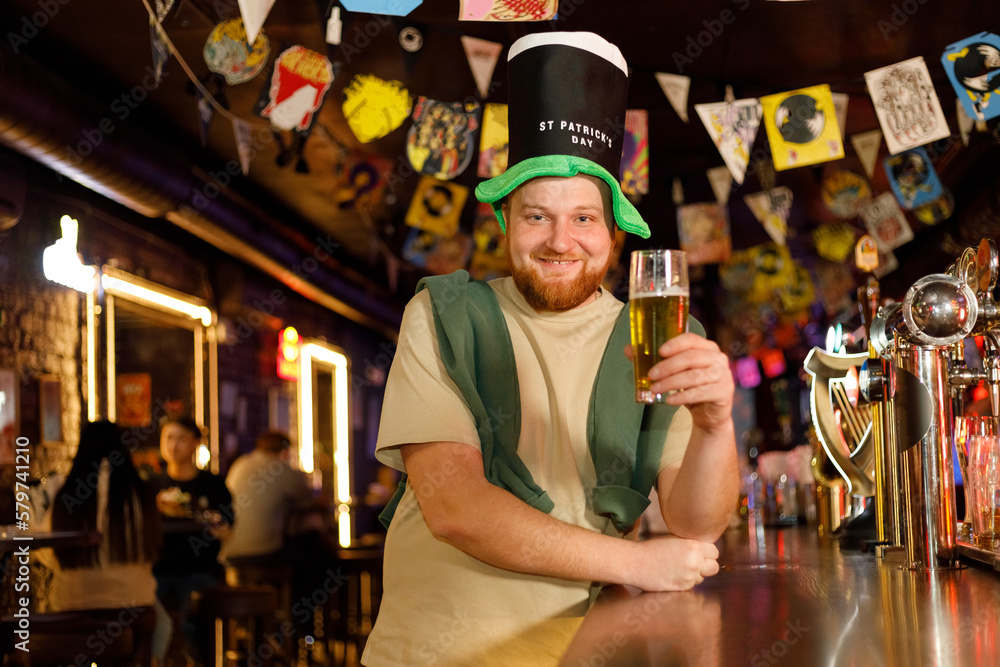 funny ginger man in leprechaun hat for st patricks day in pub with beer