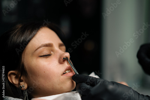 Piercing studio - a master pierces a girl's nose photo