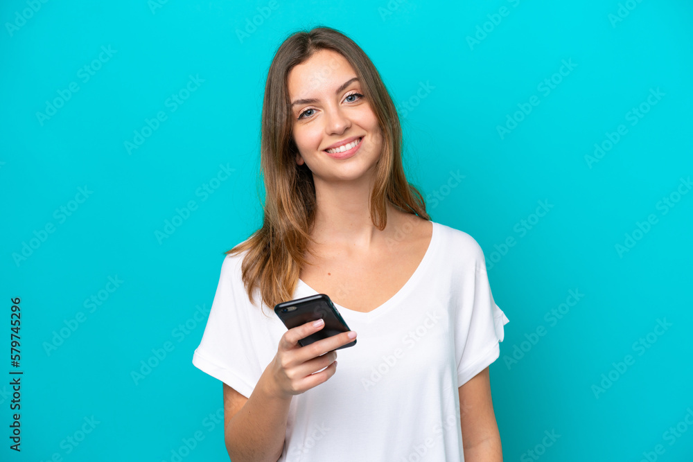 Fototapeta premium Young caucasian woman isolated on blue background using mobile phone