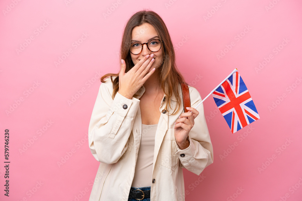 Young student caucasian woman holding an United Kingdom flag isolated on pink background happy and smiling covering mouth with hand Young student caucasian woman holding an United Kingdom flag isolated on pink background happy and smiling covering mouth with hand