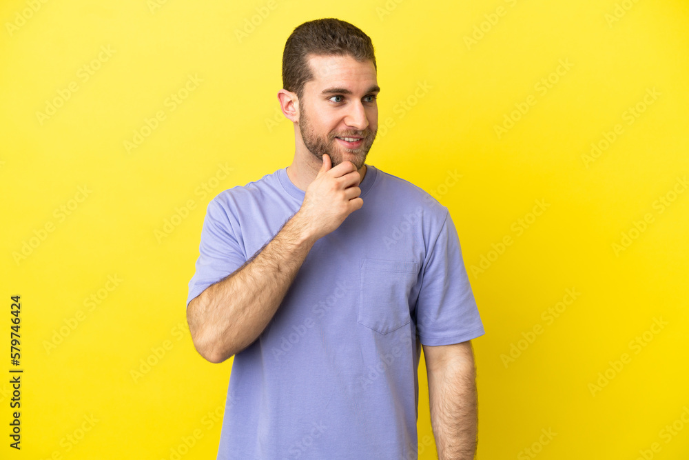 Handsome blonde man over isolated yellow background looking to the side and smiling Handsome blonde man over isolated yellow background looking to the side and smiling