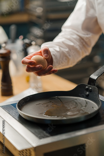 A cook breaks an egg into a pan Preparing breakfast in a professional kitchen