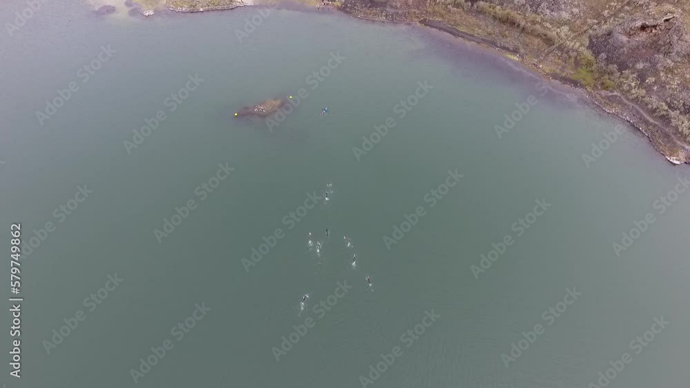 Aerial view of a group of swimmers swimming in a lake at the bottom of a volcano. The drone accompanies the athletes as they cross the Laguna Azul in Patagonia Aerial view of a group of swimmers swimming in a lake at the bottom of a volcano. The drone accompanies the athletes as they cross the Laguna Azul in Patagonia