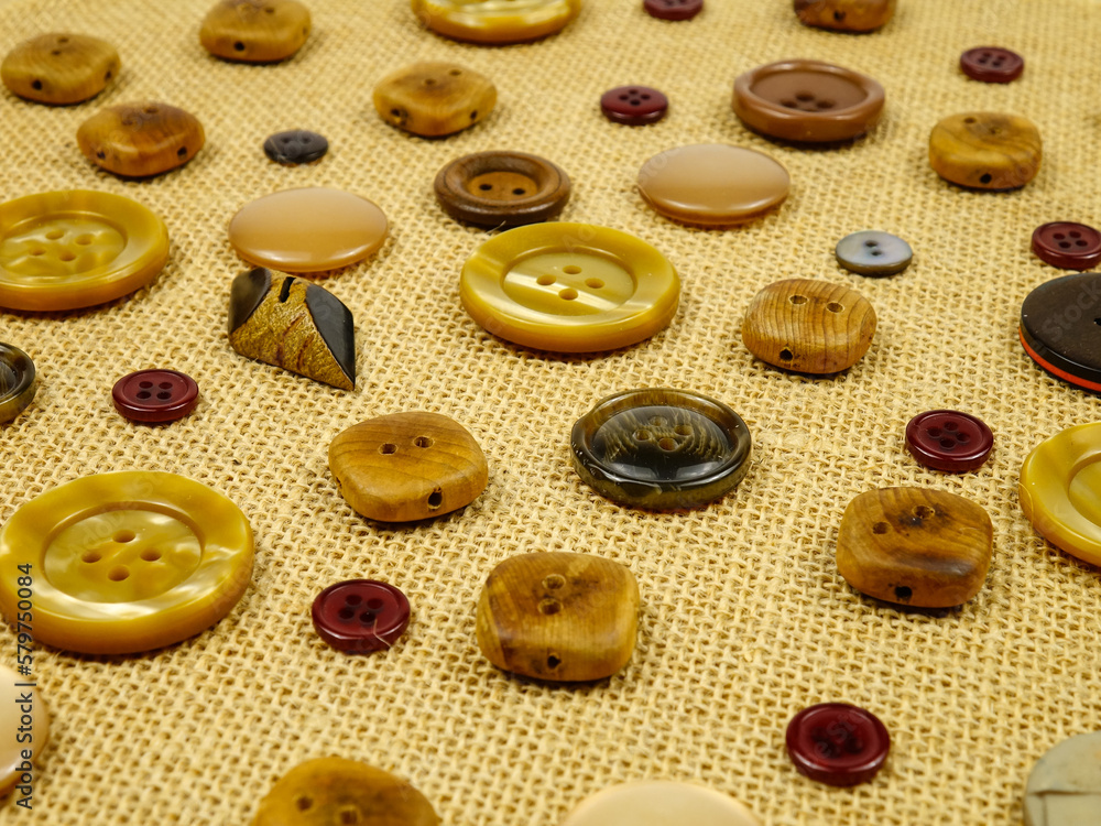 Obraz premium Brown buttons in different designs and sizes for sewing to clothes lie on the brown burlap. 