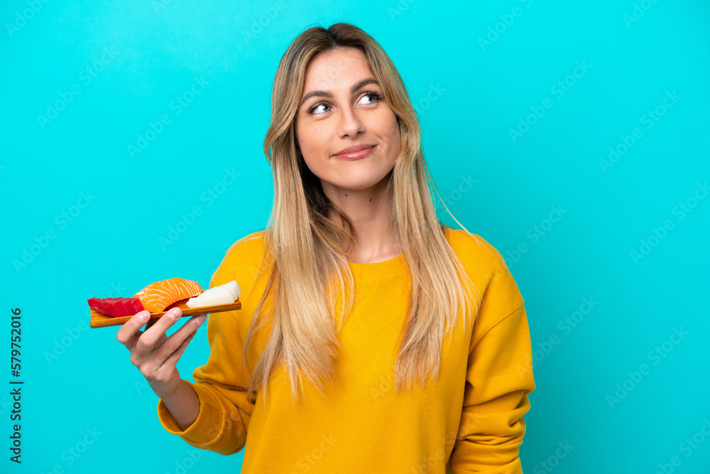 Young Uruguayan woman holding sashimi isolated on blue background thinking an idea while looking up Young Uruguayan woman holding sashimi isolated on blue background thinking an idea while looking up
