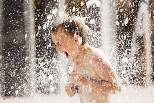 A boy playing with water in park fountain. Hot summer.