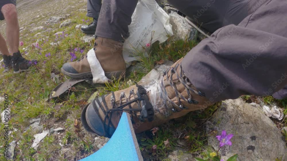 A male hiker is repairing a torn leather walking boot while camping