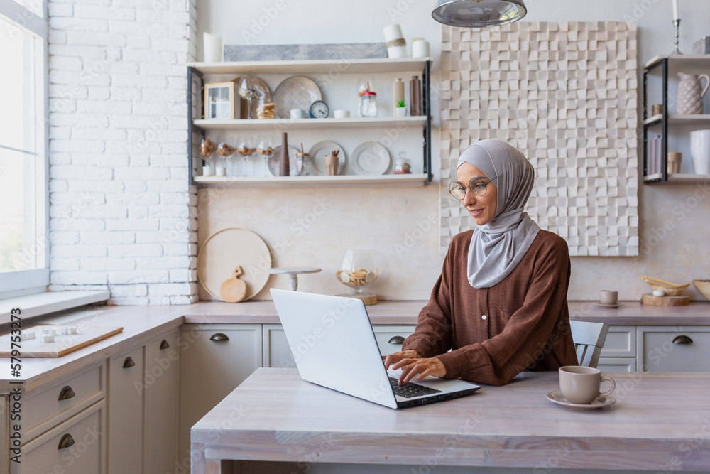 Online work from home. A young Muslim woman in a hijab sits at home in ...