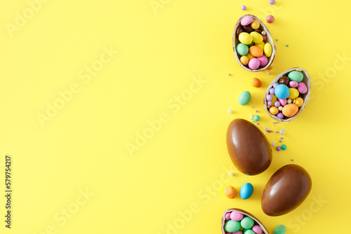 Easter sweets idea. Top view photo of chocolate eggs with сolorful dragees and sprinkles on isolated yellow background with empty space. Easter concept