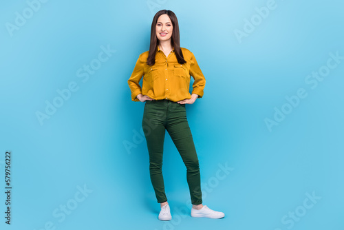 Full length photo of cheerful positive lady dressed yellow shirt standing hands arms waist isolated blue color background