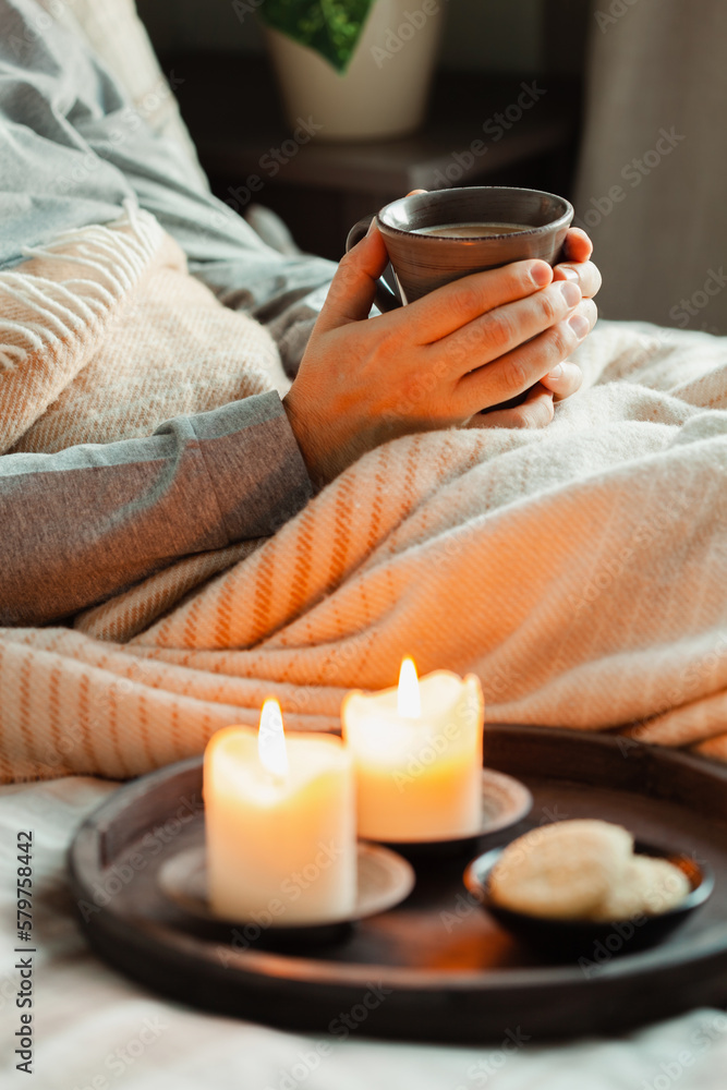 A caucasian man relaxing at home, lighting candle, drinking coffee in bed under blanket