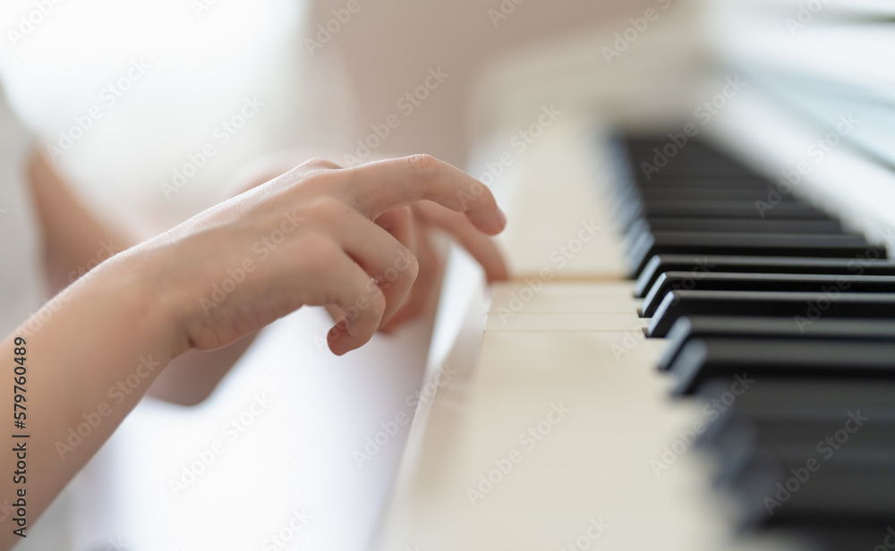 the hands of a young boy play on the keys of a white piano close-up in a bright room