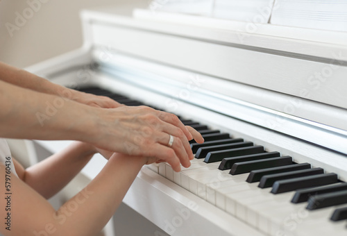 Learning to play the piano, the hands of a child and a teacher on the keys of a white piano