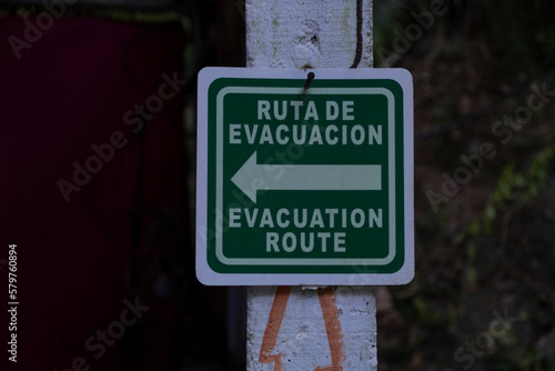 Sign in Spanish and English evacuation route with a direction arrow. Safety, danger, natural disaster concept.