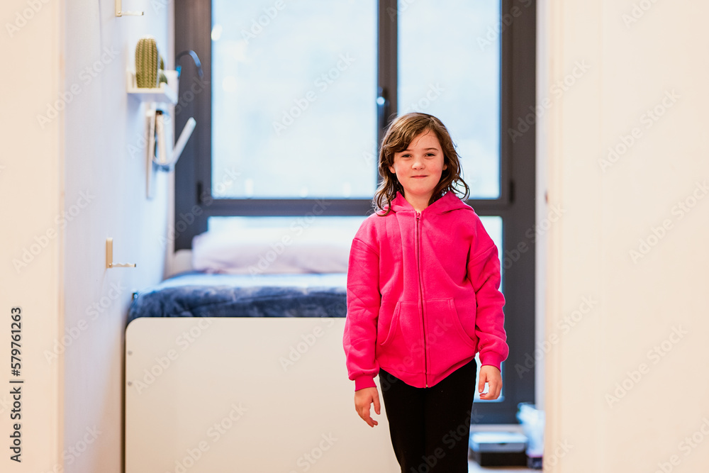 Smiling girl in pink hoodie standing near bed Smiling girl in pink hoodie standing near bed