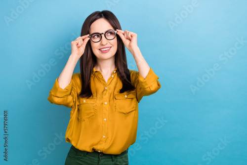 Photo of dreamy charming lady dressed yellow shirt arms eyewear looking empty space isolated blue color background