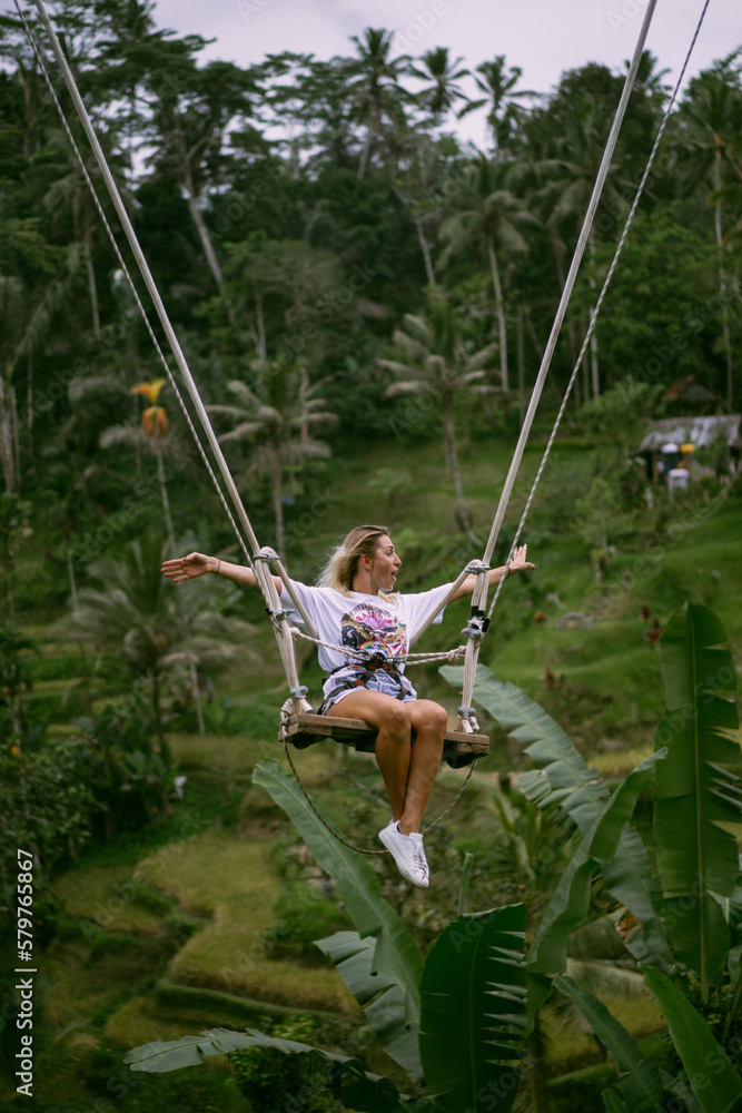 Rear view woman on a swing at vacation in Bali, Indonesia. Young girl traveler sitting on the swing in beautiful nature place in the mountains, tropical jungle view