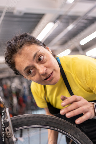 girl fixing bike listening concentrated to the noise of the wheel to make adjustments on the bike. Self-repair workshop with girl in black apron and yellow t-shirt.