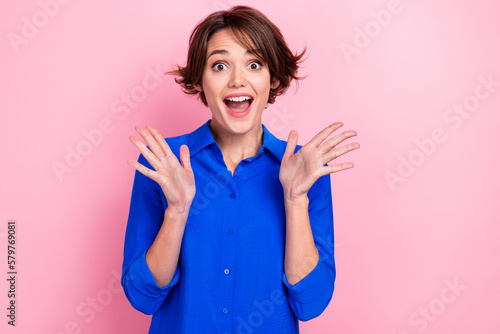 Portrait photo of young excited woman shocked hands up surprised wear blue shirt bob brown hair crazy reaction isolated on pink color background