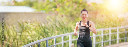 Young Asian woman runner wears fitness clothes runs in city park surrounded by trees and greenery