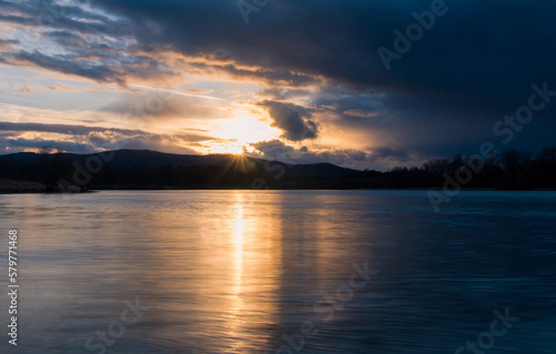 Sunset on pond with distant hill and tree silhouette. Early spring Czech landscape, long exposure