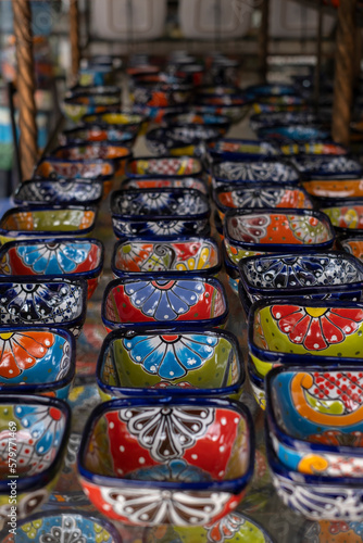 Close up of many colorful ceramic snack and sauce bowls arranged in rows at a local souvenir craft store, selective focus.