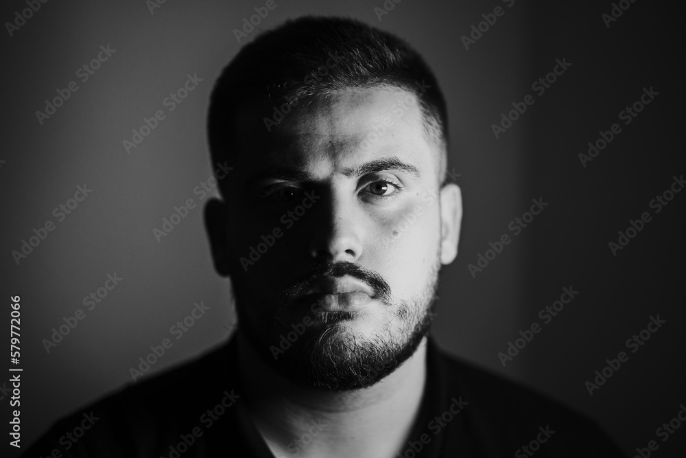 Fototapeta premium Grayscale portrait of a serious young Caucasian male with a shadow falling on his face