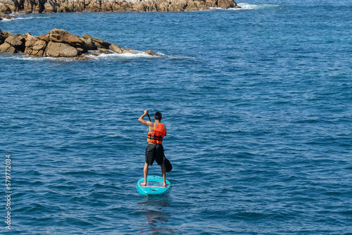 Bilde på lerret Young fit man male wearing a life vest paddling on SUP paddle board in the ocean water