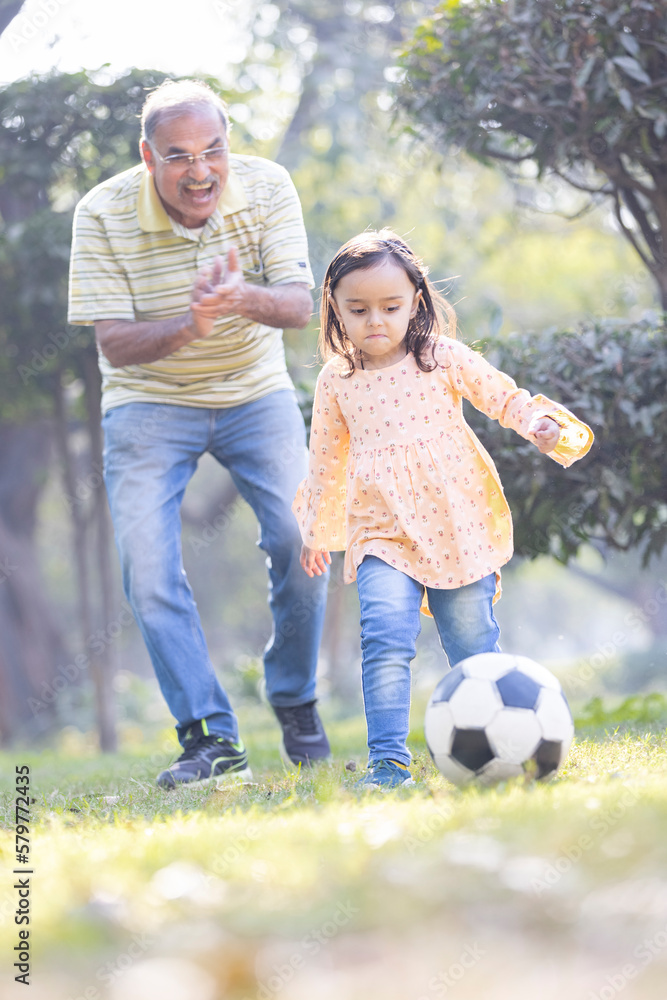 Fototapeta premium Little girl with grandfather playing football in park