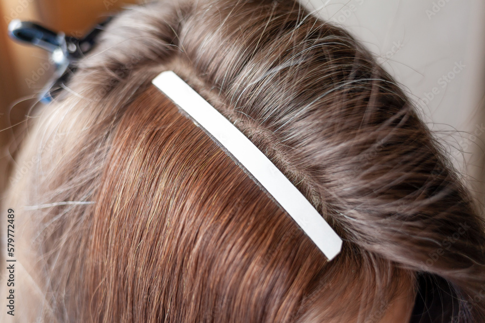 Fototapeta premium Hair ribbons for extensions on a woman's head at home. Hair extensions to thicken your own. Individual strands of hair close-up