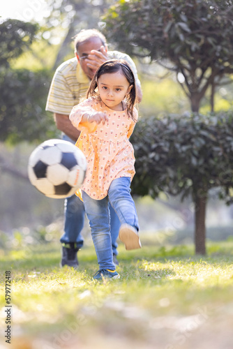 Little girl with grandfather playing football in park