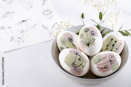 Bowl with modern creative trendy  hand painted easter egg in spring flowers on white background.  Homemade tradition Easter ideas. Greeting card photo