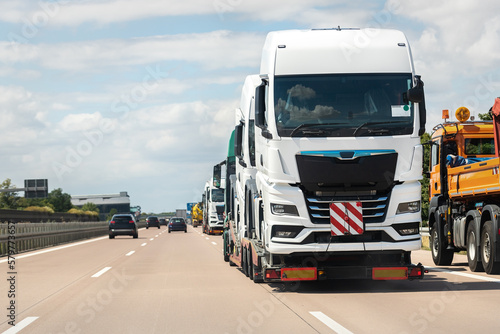 Back view of semi-trailer flatbed vehicle deliverying many new electric trucks sale automotive dealer from factory plant on highway interstate road. New business cargo transport fleet export import © Kirill Gorlov