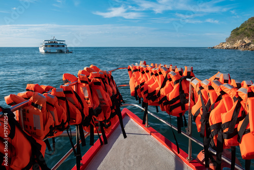 Rows of bright orange life vests hanging on tour catamaran boat railings. Blue sky and green mountains in the background.