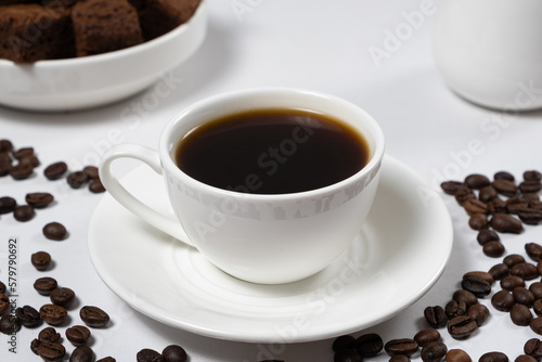 Delicious aromatic coffee in a white ceramic cup and scattered coffee beans on a white table