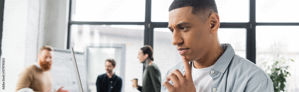 Focused african american businessman looking at laptop in office, banner. Focused african american businessman looking at laptop in office, banner.