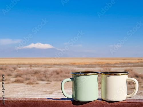 Two enameled cups of coffee or tea in the autumn landscape outdoors.Two enamel mugs in the foreground, beautiful view of the snowy mountain erciyes. Copy space for text. photo