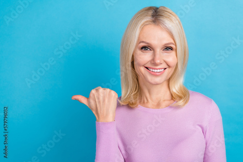 Portrait of young beautiful woman wear purple shirt directing thumb empty space shopping mall sales isolated on aquamarine color background