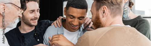 Obraz na plátne Cheerful group hugging african american man during anonymous alcoholics meeting in rehab center, banner